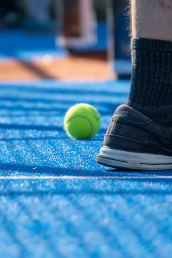 Pelota de tenis junto al calzado o zapatillas para pádel.